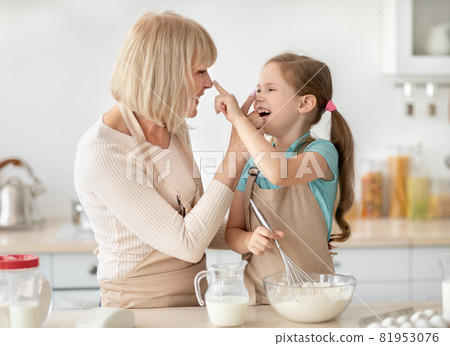Mature woman and girl cooking playing with flour touching noses Mature woman and girl cooking playing with flour touching noses 81953076