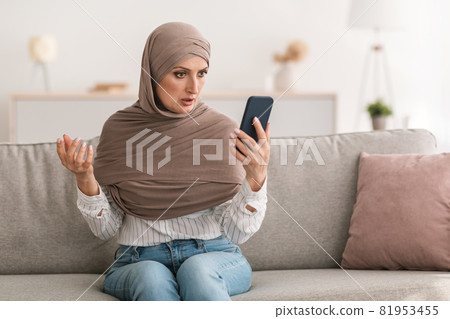 Shocked Mature Islamic Woman Holding Phone Reading Negative Message Indoors 81953455