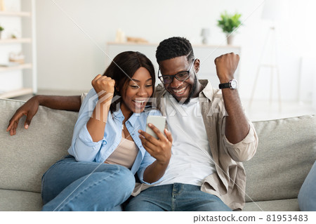 African american couple using cellphone, celebrating win African american couple using cellphone, celebrating win 81953483