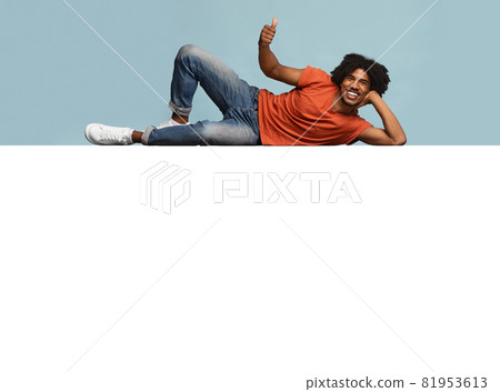 Relaxed black guy reclining on huge empty placard over blue 81953613