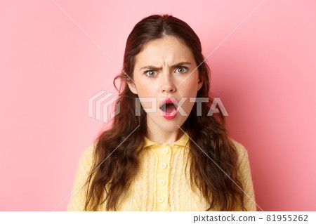 Shocked and hurt young woman frowning, staring offended and disappointed, gasping, looking judgemental, standing over pink background 81955262