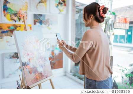 asian female artist taking picture of her own painting using smartphone 81958536