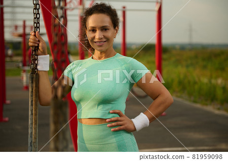 Confident portrait of athlete woman of mixed race with healthy aesthetic body wearing in sportswear smiling looking at camera, enjoying the morning bodyweight training in the outdoor sportsground 81959098