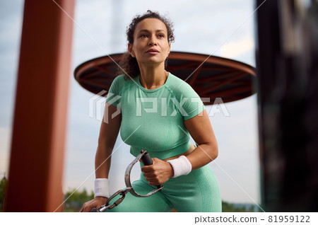 Sporty determinate African American, Latin American, Hispanic female athlete performing a weight training with stationary cable crossover equipment in the sportsground outdoor. Bodybuilding concept 81959122
