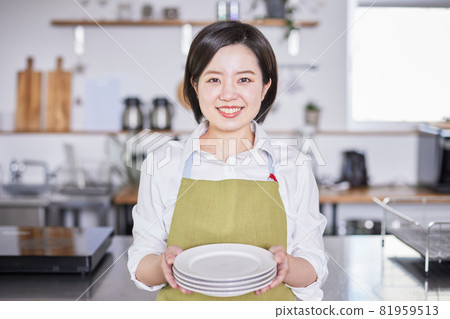 一個穿著圍裙的年輕女子站在廚房裡的盤子裡 一個穿著圍裙的年輕女子站在廚房裡的盤子裡 81959513