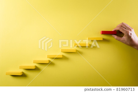 Concept of building success foundation. Hand holding wooden block stacking as step stair, Success in business growth concept on yellow background. 81960713