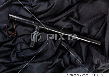 black rubber police baton on black shirt wrinkled cloth low-key flat lay black rubber police baton on black shirt wrinkled cloth low-key flat lay 81961839
