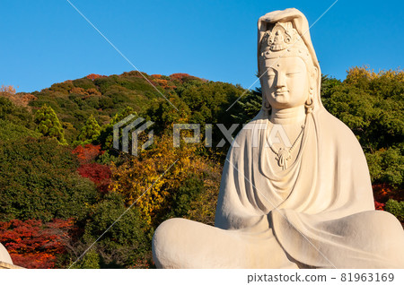 Giant statue of Ryozen Kannon Bodhisattva Avalokiteshvara, illuminated by amazing sunlight, autumn mountains, blue sky. Giant statue of Ryozen Kannon Bodhisattva Avalokiteshvara, illuminated by amazing sunlight, autumn mountains, blue sky. 81963169