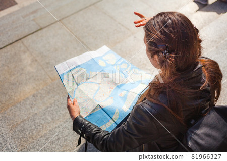 Young woman looking at paper map of Venice and thinking about her trip on sunny day 81966327