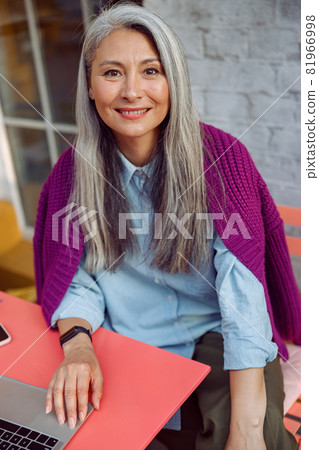 Portrait of happy senior Asian woman with laptop sitting at coral table on outdoors cafe terrace 81966998