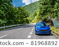 A blue car and a green forest parked on the side of a mountain road in midsummer 81968892