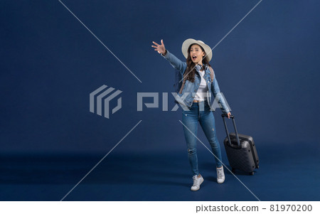 Happy young Asian woman holding baggage and hurry up to airport on blue color background, carry backpacker and wearing headphone, holiday and vacation, travel and tourist concept Happy young Asian woman holding baggage and hurry up to airport on blue color background, carry backpacker and wearing headphone, holiday and vacation, travel and tourist concept 81970200
