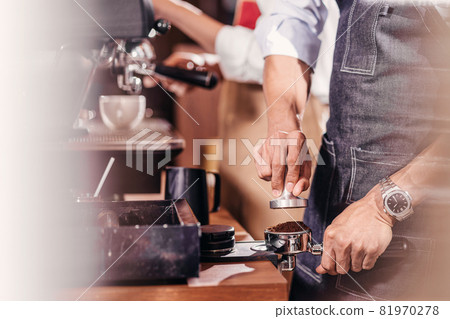 Closeup Asian Barista tamping the portafilter and preparing cup of coffee, espresso with latte or cappuccino for customer order in coffee shop, Small business owner and startup in coffee shop concept. Closeup Asian Barista tamping the portafilter and preparing cup of coffee, espresso with latte or cappuccino for customer order in coffee shop, Small business owner and startup in coffee shop concept. 81970278