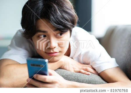 Young man looking at a smartphone on the couch 81970768