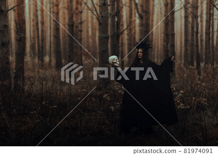 black terrible witch with a skull in the hands of a dead man performs an occult mystical ritual 81974091