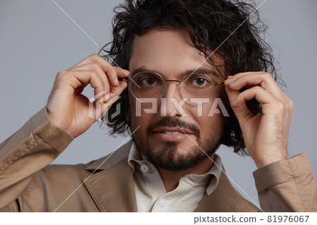 indoor portrait of handsome freckled smiling male with curly hair, wears sepctacles posing for social advertisement, isolated on gray wall with copy space for your promotional information indoor portrait of handsome freckled smiling male with curly hair, wears sepctacles posing for social advertisement, isolated on gray wall with copy space for your promotional information 81976067