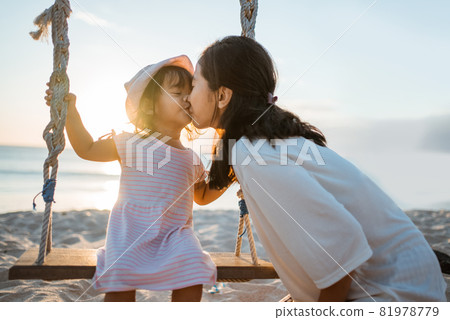 daughter kissing her mother while swinging at the beach daughter kissing her mother while swinging at the beach 81978779