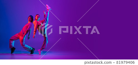 Flyer. Two dancers, young man and woman dancing hip-hop in casual sports youth clothes on gradient purple pink background at dance hall in neon light. 81979406