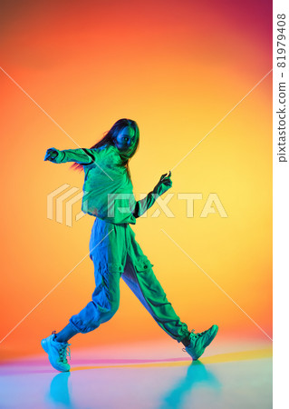 Young sportive girl dancing hip-hop in stylish clothes on colorful background at dance hall in neon light. Youth culture, movement, style and fashion, action. Young sportive girl dancing hip-hop in stylish clothes on colorful background at dance hall in neon light. Youth culture, movement, style and fashion, action. 81979408