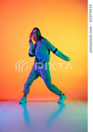 Young sportive girl dancing hip-hop in stylish clothes on colorful background at dance hall in neon light. Youth culture, movement, style and fashion, action. 81979418