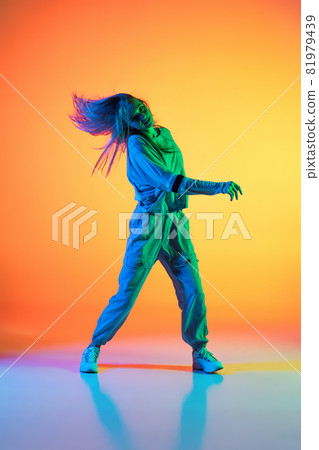 One Caucasian sportive girl dancing hip-hop in stylish clothes on colorful background at dance hall in neon light. Youth culture, movement, style and fashion, action. One Caucasian sportive girl dancing hip-hop in stylish clothes on colorful background at dance hall in neon light. Youth culture, movement, style and fashion, action. 81979439