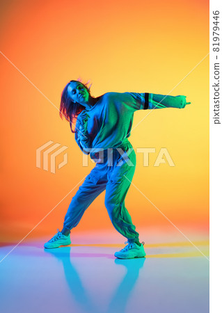 One Caucasian sportive girl dancing hip-hop in stylish clothes on colorful background at dance hall in neon light. Youth culture, movement, style and fashion, action. One Caucasian sportive girl dancing hip-hop in stylish clothes on colorful background at dance hall in neon light. Youth culture, movement, style and fashion, action. 81979446
