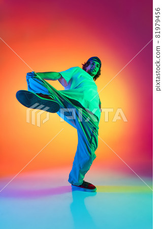 Conceptual portrait of young man, hip-hop dancer in stylish clothes in action isolated on colorful background at dance hall in neon light. Conceptual portrait of young man, hip-hop dancer in stylish clothes in action isolated on colorful background at dance hall in neon light. 81979456
