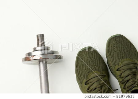 pair of green textile sneakers and a metal dumbbell on a white background, top view. pair of green textile sneakers and a metal dumbbell on a white background, top view. 81979635