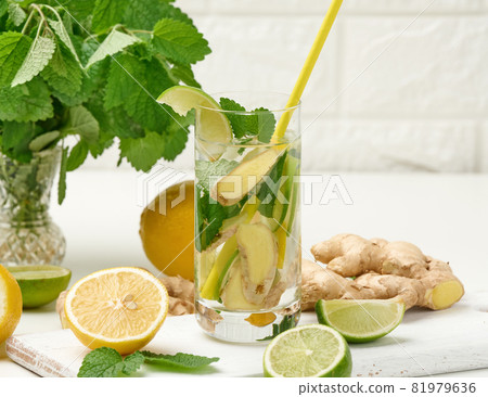 transparent glass cup with lemon, lime pieces and mint leaves and ginger pieces on a white table, detox. transparent glass cup with lemon, lime pieces and mint leaves and ginger pieces on a white table, detox. 81979636
