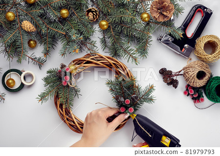 Female hands decorate the Christmas wreath with spruce branches with a red berry and forest cones. White background. New Year's concept. 81979793