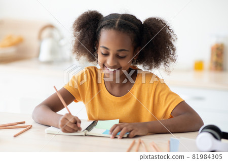 Cheerful african american teen girl doing homework at kitchen 81984305
