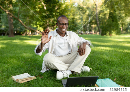 E-learning concept. African american student guy using laptop and having distant online lecture, sitting in park 81984515