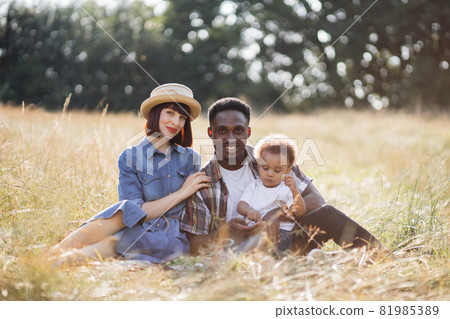 Multi ethnic family of three sitting on grass during picnic 81985389