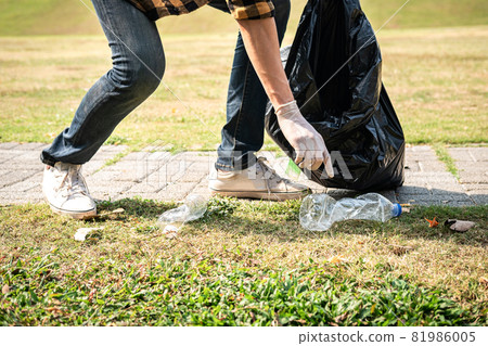 Volunteer man in gloves walking and stopping to collect plastic bottles into plastic black bag for cleaning the park 81986005