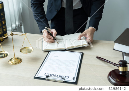 Counselor lawyer or notary working on a documents and report of the important case and wooden gavel, brass scale on table in courtroom 81986142