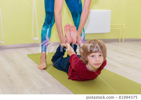 A woman instructor in a sports uniform is engaged in yoga with a boy. 81994375