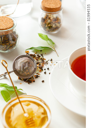 Cup of hot black tea on white table with dry tea jar 81994535