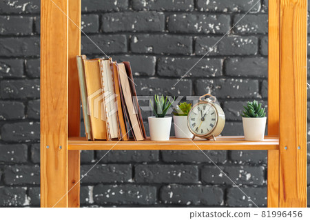 Wooden bookshelf with books and stuff against black brick wall Wooden bookshelf with books and stuff against black brick wall 81996456