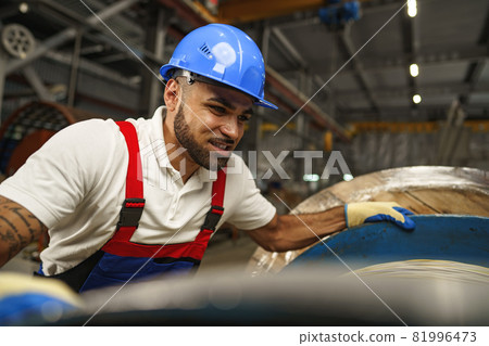 A young factory workman rolls heavy coil of electric cable 81996473
