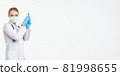 A young nurse in a mask and white coat holds a syringe with a needle for injections, flu shots 81998655