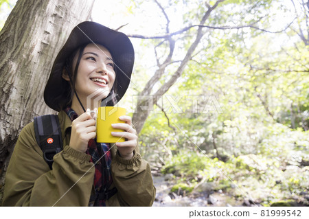 Trekking image of a woman sitting in an outdoor chair and drinking a drink Trekking image of a woman sitting in an outdoor chair and drinking a drink 81999542