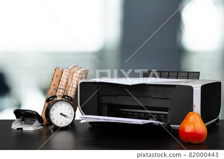 Compact home printer on desk with books against blurred background 82000443