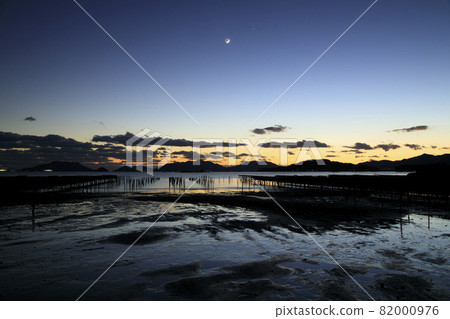 The sunset sky and the setting crescent moon in the winter Setouchi lined with oyster shelves 82000976