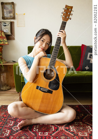 Young woman playing the guitar in the room 82002281