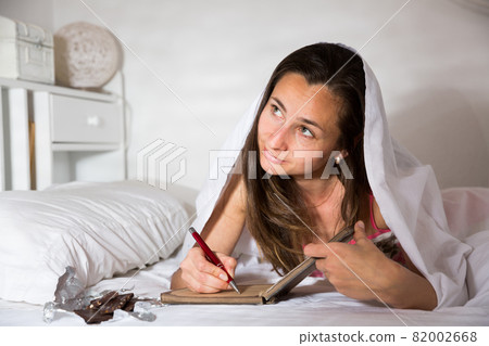 Woman elaxing under blanket and making schedule for tomorrow Woman elaxing under blanket and making schedule for tomorrow 82002668