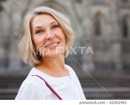 Cheerful mature female is walking in white blouse on the street outdoor 82002961