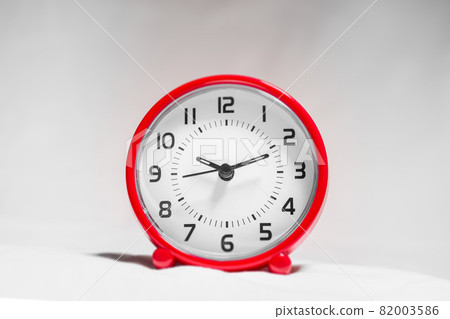 Small red alarm clock show the running time. A modern clock with red frame. Smile face of a clock. Close up on a red plastic watch with second pointer on white background. Ten after twelve . 82003586