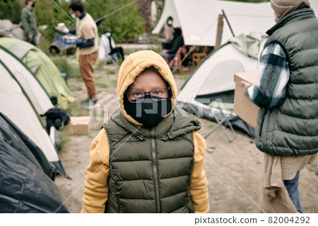 Portrait of mixed race child in hoodie, vest, eyeglasses and cloth mask standing in refugee camp Portrait of mixed race child in hoodie, vest, eyeglasses and cloth mask standing in refugee camp 82004292