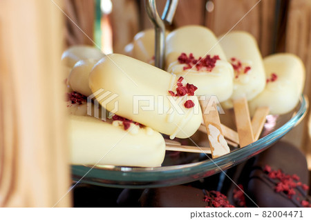 Cake pops in white chocolate in the shape of a mini ice cream on a stick. Cake pops are garnished with dry strawberry crumbs. Selective focus Cake pops in white chocolate in the shape of a mini ice cream on a stick. Cake pops are garnished with dry strawberry crumbs. Selective focus 82004471