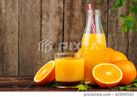 Bottle of orange juice with oranges on wooden table 82004583